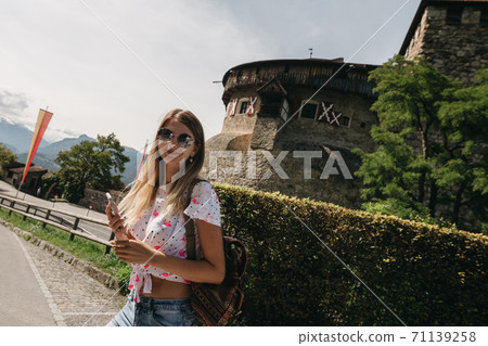 Beautiful portrait of a smiling young girl in stylish glasses.Traveling girl with a backpack on his shoulders.Woman model appearance on the background of the ancient castle.Liechtenstein,Schloss Vaduz Beautiful portrait of a smiling young girl in stylish glasses.Traveling girl with a backpack on his shoulders.Woman model appearance on the background of the ancient castle.Liechtenstein,Schloss Vaduz 71139258