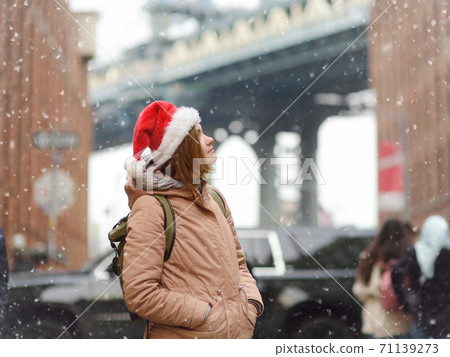 A young woman tourist in a Santa Claus hat walks during a snowfall in New York City on Christmas Eve A young woman tourist in a Santa Claus hat walks during a snowfall in New York City on Christmas Eve 71139273