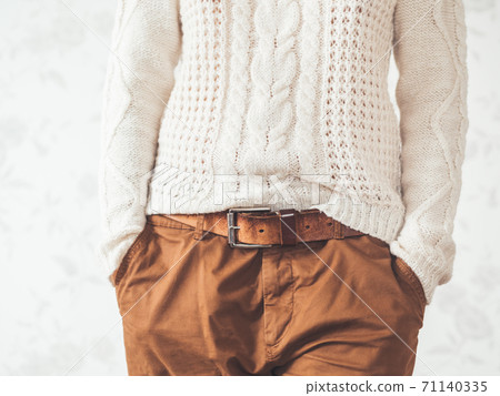 Woman in cable-knit white sweater with Scandinavian pattern and brown chinos trousers with leather belt. Casual clothes for snuggle weather. Modern urban fashion. 71140335
