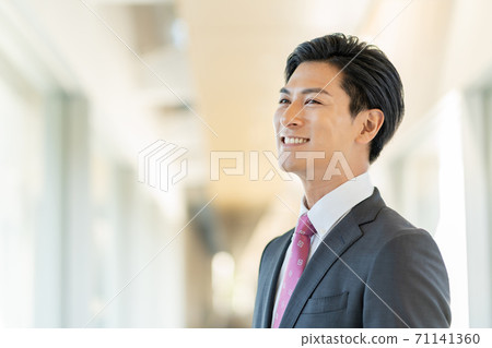 站立在辦公室走廊的一個年輕微笑的人 站立在辦公室走廊的一個年輕微笑的人 71141360