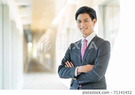 A young smiling man standing in the office corridor with his arms folded A young smiling man standing in the office corridor with his arms folded 71141452