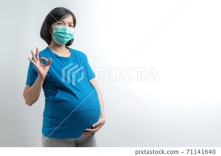 Smiling Asian Pregnant woman wearing protective face mask showing gesture OK sign 71141640