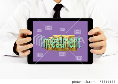 Businessman holding a tablet with green word Investment and golden coins stacks and laptop icons 71144411