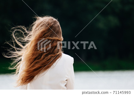 Woman standing looking at the lake. The hair was blown away by the wind. 71145993