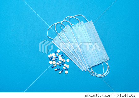 Protective medical face masks and pills on a blue background - Top view with copy space Protective medical face masks and pills on a blue background - Top view with copy space 71147102