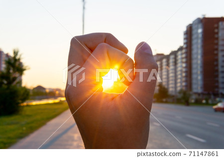 human hand covers the sunlight, the sun shines through the hand. urban landscape. selective focus human hand covers the sunlight, the sun shines through the hand. urban landscape. selective focus 71147861