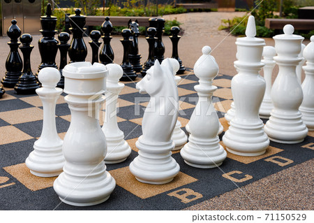 Outdoor chess board with big plastic pieces. Giant size chess in public area zone. Close up big pieces and giant chess board of street chess in the park 71150529