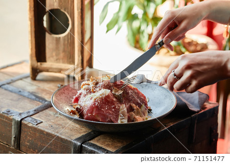 A female hand is preparing a vegetable salad with beef roast beef. A plate of salad with beef roast beef, onions, arugula, pepper and tomatoes on a black table. Top view. 71151477