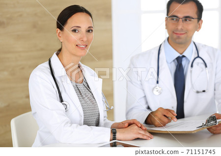 Middle aged woman doctor filling up medical documents or prescription with her male colleague. Group of doctors at work discussing treatment problems while sitting at a desk in hospital. Data in Middle aged woman doctor filling up medical documents or prescription with her male colleague. Group of doctors at work discussing treatment problems while sitting at a desk in hospital. Data in 71151745
