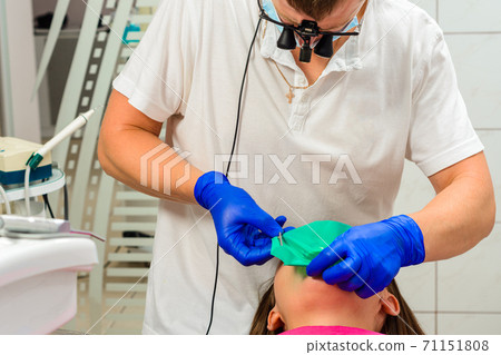 Installation of a rubber dam with a metal clamp for dental fillings, sterile and modern dental treatment. Installation of a rubber dam with a metal clamp for dental fillings, sterile and modern dental treatment. 71151808