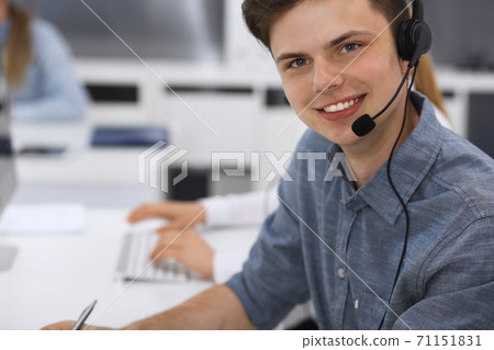 Call center. Group of casual dressed operators at work. Focus on young businessman in headset at customer service office. Telesales in business Call center. Group of casual dressed operators at work. Focus on young businessman in headset at customer service office. Telesales in business 71151831