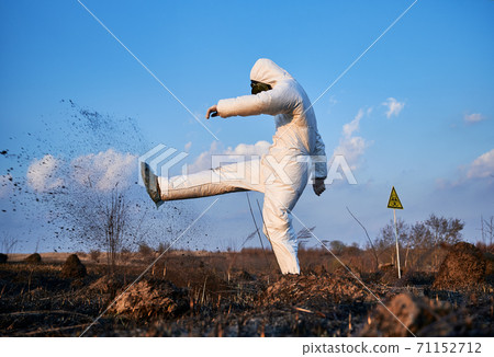 Lab worker in a protective costume working in scorched field Lab worker in a protective costume working in scorched field 71152712