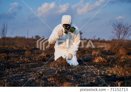 Ecologist examining soil in field after fire. Ecologist examining soil in field after fire. 71152713