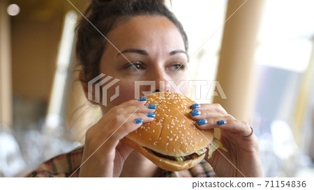 Young Hungry Woman holding Vegan Meatless Burger in Fast Food Restaurant. close-up shot. Fast food eats. Burger in female hands. 71154836
