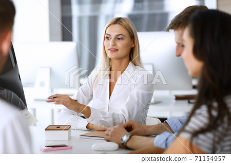 Group of business people discussing questions at meeting. Headshot of blonde businesswoman while smiling to her colleague at office negotiation. Teamwork and cooperation in corporate occupation 71154957