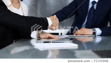 Business people shaking hands after contract signing at the glass desk in modern office. Unknown businessman with colleagues at meeting or negotiation. Teamwork, partnership and handshake concept Business people shaking hands after contract signing at the glass desk in modern office. Unknown businessman with colleagues at meeting or negotiation. Teamwork, partnership and handshake concept 71155946