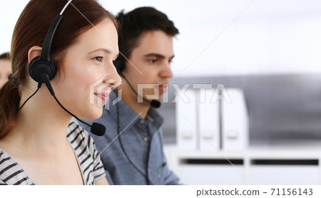 Group of operators at work. Call center. Focus on beautiful woman receptionist in headset at customer service. Business concept and casual striped clothing style 71156143
