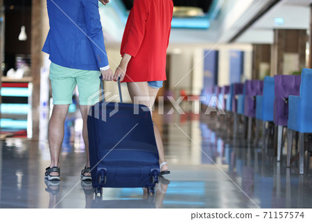 Man and woman stand with their backs and hold on to handle of suitcase. 71157574