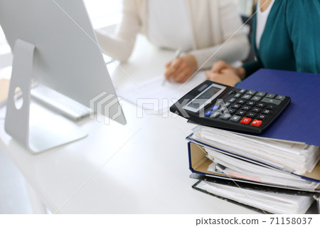 Calculator and binders with papers are waiting to be processed by business woman or bookkeeper working at the desk in office back in blur. Internal Audit and tax concept 71158037