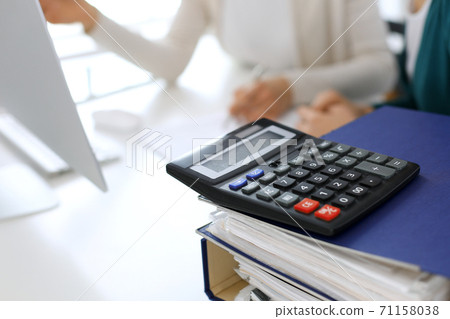 Calculator and binders with papers are waiting to be processed by business woman or bookkeeper working at the desk in office back in blur. Internal Audit and tax concept 71158038