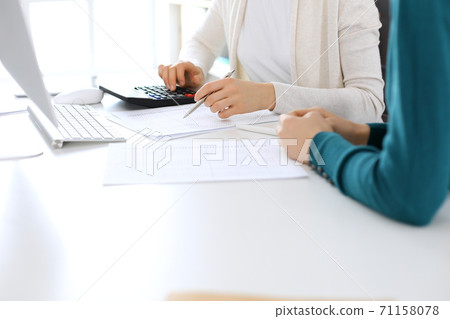 Accountant checking financial statement or counting by calculator income for tax form, hands close-up. Business woman sitting and working with colleague at the desk in office. Audit concept Accountant checking financial statement or counting by calculator income for tax form, hands close-up. Business woman sitting and working with colleague at the desk in office. Audit concept 71158078