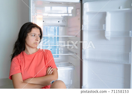 The girl is surprised at the empty refrigerator. Lack of food. Food delivery The girl is surprised at the empty refrigerator. Lack of food. Food delivery 71158153