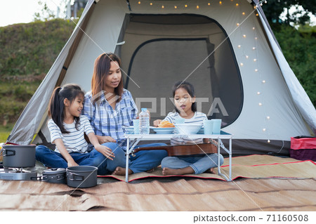Asian mother and two child girls having fun to picnic outside tent in the camping site in the beautiful nature. Family enjoy with nature and camping concept. Asian mother and two child girls having fun to picnic outside tent in the camping site in the beautiful nature. Family enjoy with nature and camping concept. 71160508