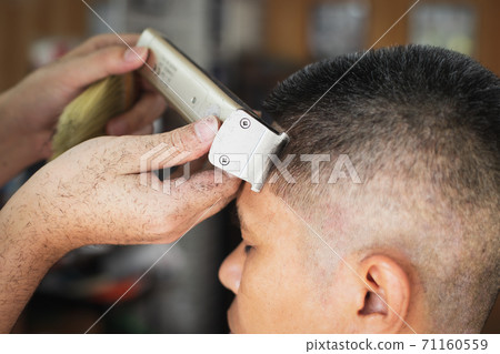 Asian young man who have gray hair being haircut with electric clipper machine by professional barber in barbershop. 71160559