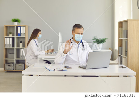 Doctors in face masks having video calls with patients or answering questions on online chats 71163315