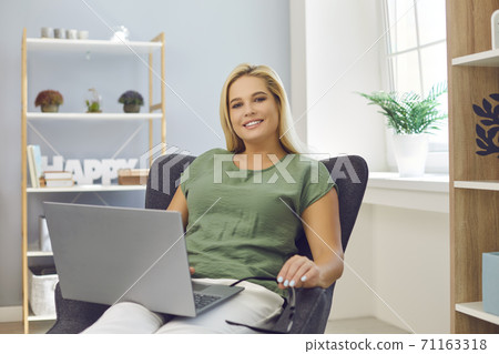 Successful self-made woman sitting in an armchair with laptop computer in her home office 71163318