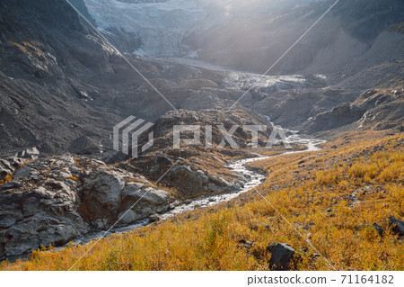 Rocky mountains, glacier and autumnal grass. High mountain landscape with river Rocky mountains, glacier and autumnal grass. High mountain landscape with river 71164182