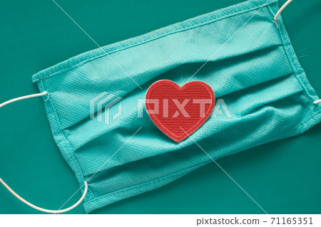 Close up of blue surgical masks and heart symbol on green Close up of blue surgical masks and heart symbol on green 71165351
