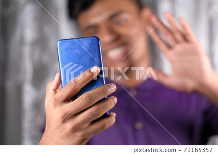 Smiling young man using his phone to make a video call Smiling young man using his phone to make a video call 71165352