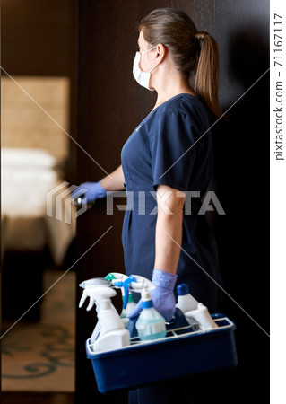Housemaid in mask at the entrance to the hotel room 71167117
