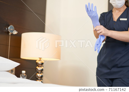 Housemaid in mask using protective gloves in hotel room 71167142