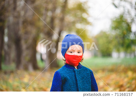 Concept of new normal with little girl in red mask and warm clothes walking in autumn park Concept of new normal with little girl in red mask and warm clothes walking in autumn park 71168157