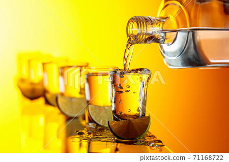 Tequila with lime slices on a yellow background. Tequila with lime slices on a yellow background. 71168722