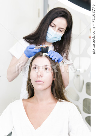 The doctor dermatologist examining client hair with a special apparatus for diagnostic hair. 71168779