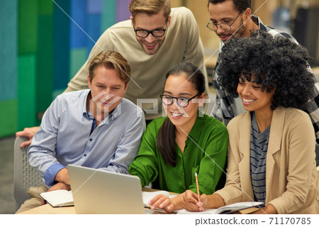 Group of happy multiracial business people sitting at desk in the modern coworking space, looking at laptop screen and smiling, working together Group of happy multiracial business people sitting at desk in the modern coworking space, looking at laptop screen and smiling, working together 71170785