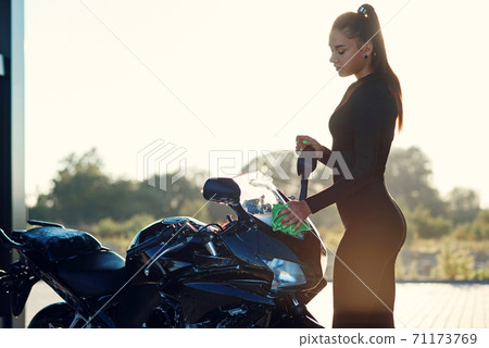 Seductive young woman washing stylish sport motorcycle and wipes it from purple foam. Taking care about vehicle. Seductive young woman washing stylish sport motorcycle and wipes it from purple foam. Taking care about vehicle. 71173769