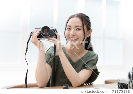一個微笑的少婦在她的手上的拿著影片單鏡頭反光照相機 71175128