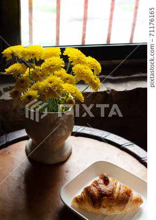 homemade fresh croissant serves on white plate for the client's morning breakfast on wooden table near the window with yellow flower decoration at the coffee shop. low key food and bakery photo style. 71176165