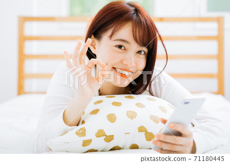 一個女人躺在床上,使用智能手機 一個女人躺在床上,使用智能手機 71180445