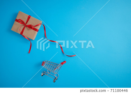 Gift box with shopping cart on blue background. Gift box with shopping cart on blue background. 71180446