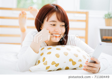 一個女人躺在床上,使用智能手機 一個女人躺在床上,使用智能手機 71180449