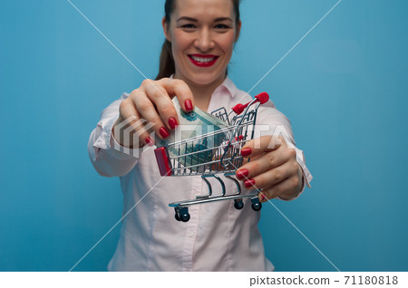 Young woman with a toy grocery basket with a bundle of rubles in her hands. 71180818