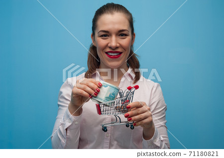 Young woman with a toy grocery basket with a bundle of rubles in her hands. 71180821