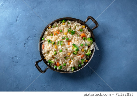 Vegetable stir fried rice, overhead shot on a blue background. Basmati with broccoli, green peas and carrots Vegetable stir fried rice, overhead shot on a blue background. Basmati with broccoli, green peas and carrots 71182855
