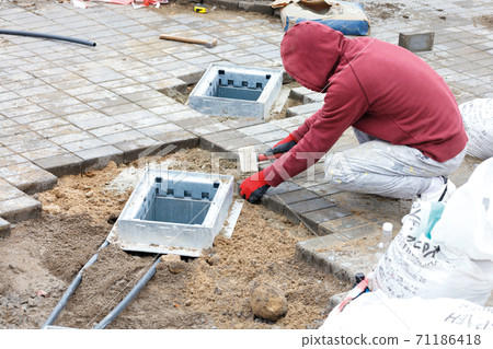 A worker installs utility shafts and lays paving slabs around them. 71186418