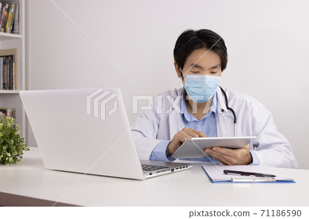 Asian Doctor and Stethoscope Wear Face Mark Using Digital Tablet in Office 71186590